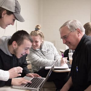 Friar and a group of students looking at a laptop in a classroom