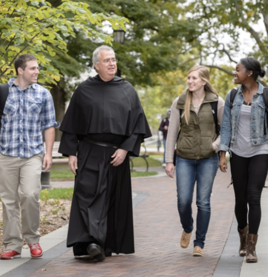 Friar walking with three college students through a college campus