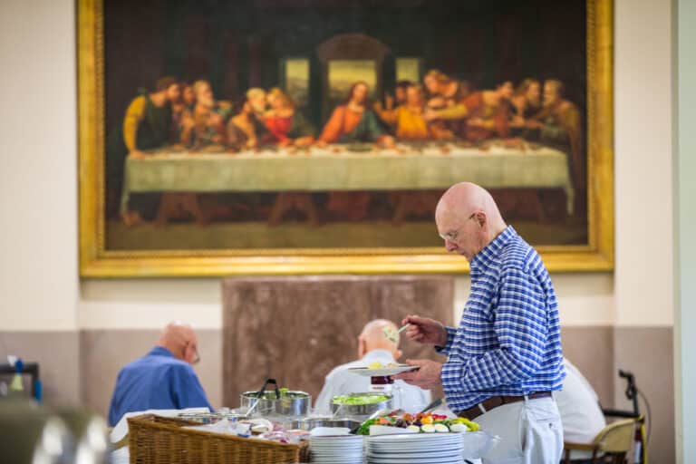 An elderly friar assembling a plate of food in a monastery.
