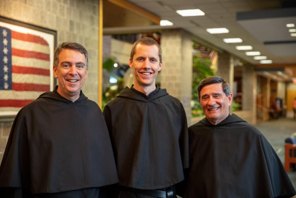 Three smiling men in black Augustinian robes standing together
