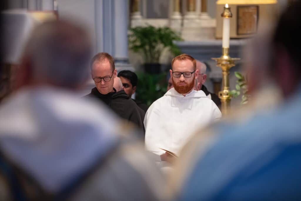 Two Augustinian vocations at a ceremony with their eyes closed and heads bowed.