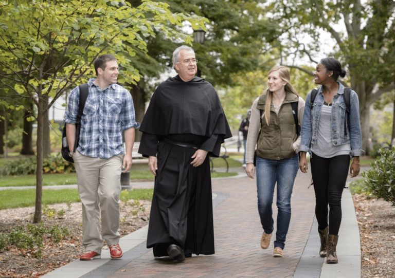 Friar walking with three college students through a college campus